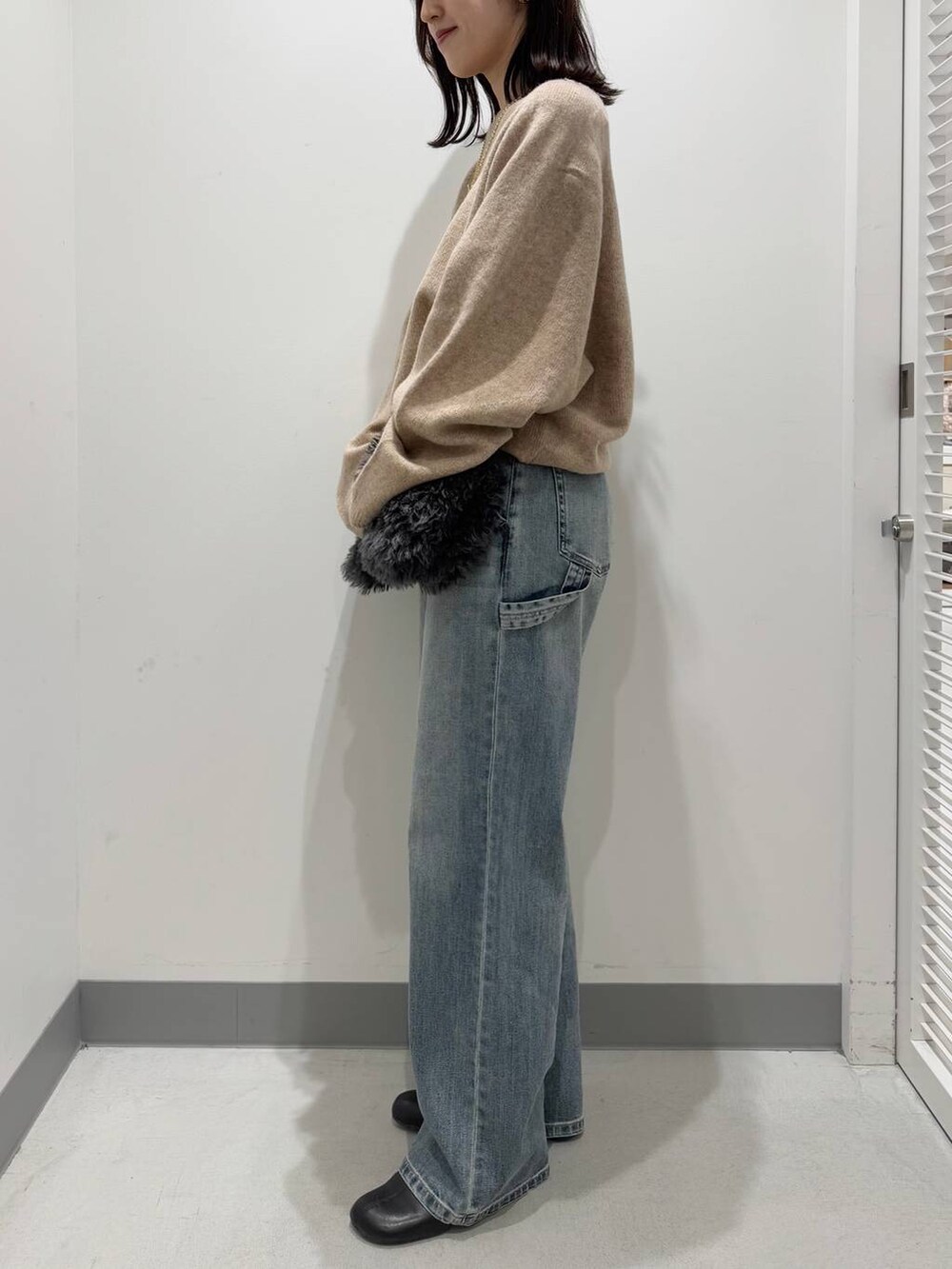 グレー系のトートバッグ、ブラック系のブーツ、ブルー系のデニムパンツを着用したレディースの冬コーディネートの2枚目の写真