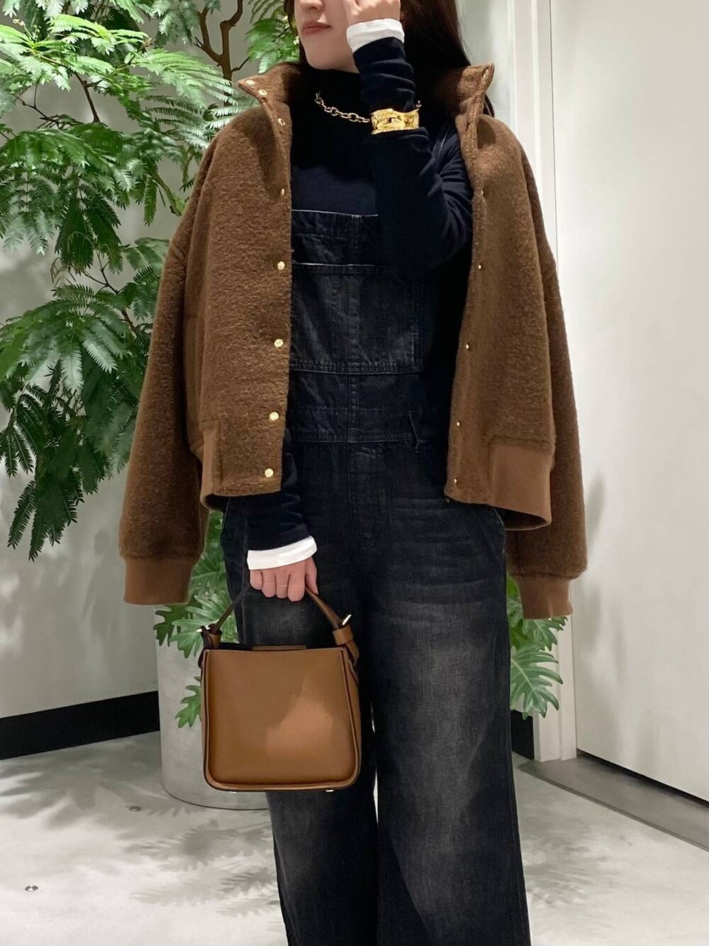 ブラウン系のハンドバッグ、ホワイト系のTシャツ/カットソー、ブラック系のサロペット/オーバーオールを着用したレディースの秋コーディネートの2枚目の写真