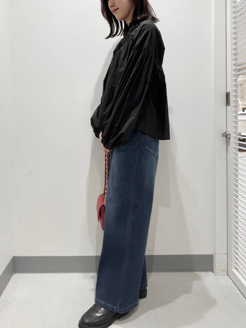 ブルー系のデニムパンツ、ブラック系のローファー、レッド系のハンドバッグを着用したレディースの冬コーディネートの2枚目の写真