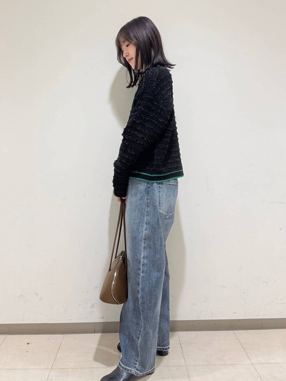 イエロー系のトートバッグ、ブルー系のデニムパンツ、ブラック系のブーツを着用したレディースの冬コーディネートの2枚目の写真