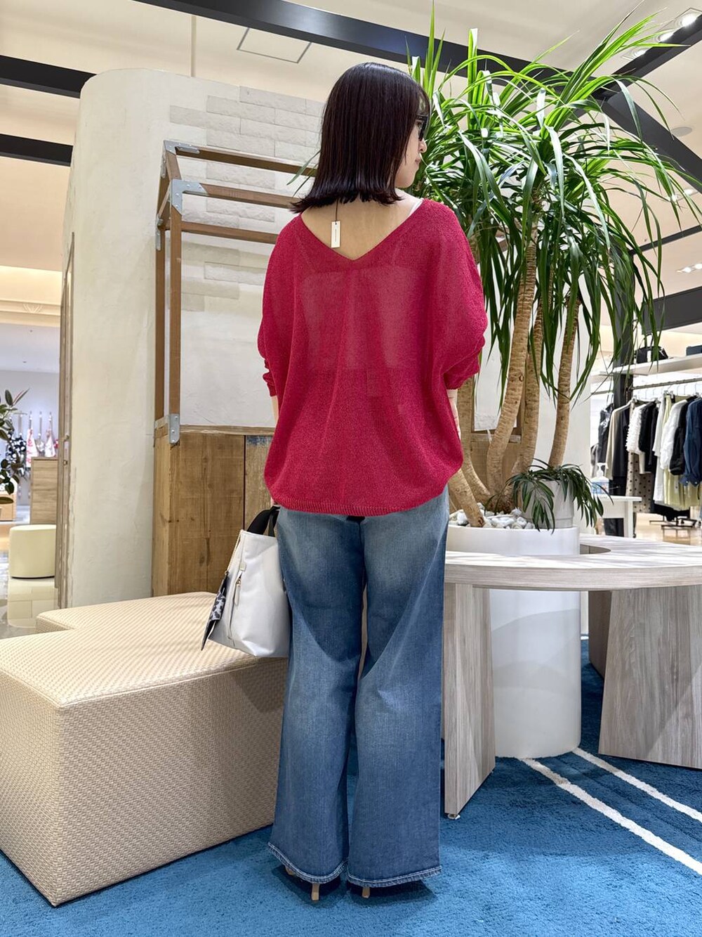 ホワイト系のトートバッグ、ブルー系のデニムパンツ、レッド系のニット/セーターを着用したレディースの春コーディネートの2枚目の写真