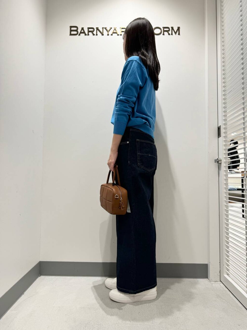 ブルー系のニット/セーター、ブルー系のデニムパンツ、ブラウン系のハンドバッグを着用したレディースの冬コーディネートの2枚目の写真