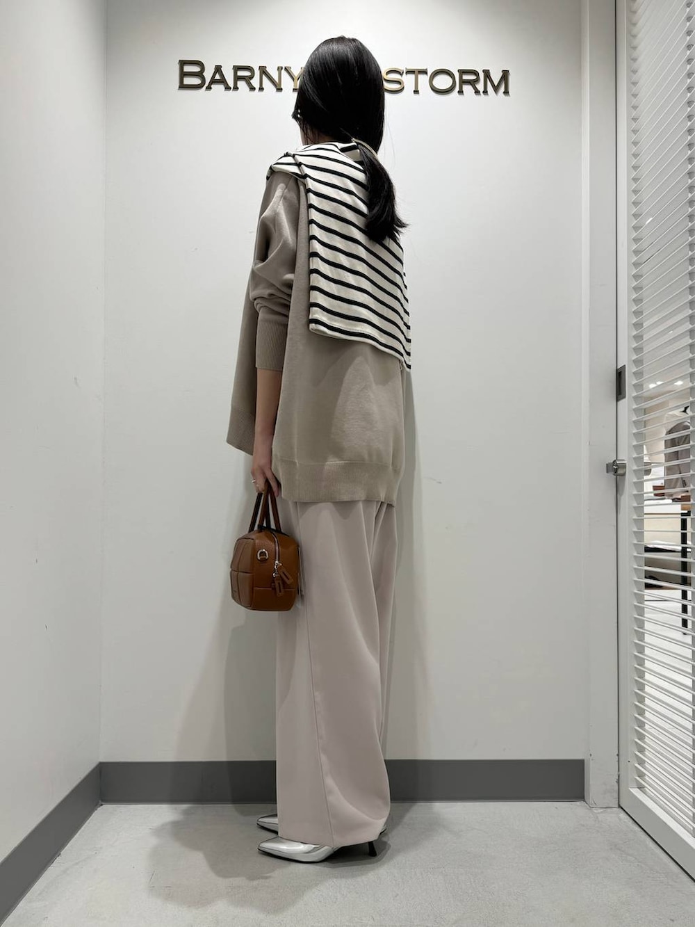 シルバー系のパンプス、イエロー系のスラックス、ブラウン系のハンドバッグを着用したレディースの冬コーディネートの2枚目の写真