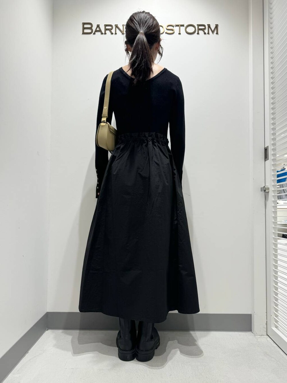 ブラック系のワンピース、ブラック系のブーツ、ベージュ系のショルダーバッグを着用したレディースの冬コーディネートの4枚目の写真