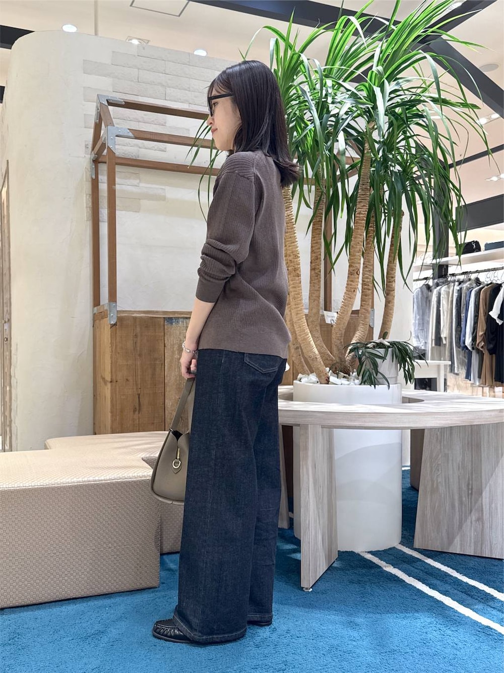 ブラック系のハンドバッグ、ブラック系のローファー、ブルー系のデニムパンツを着用したレディースの秋コーディネートの2枚目の写真