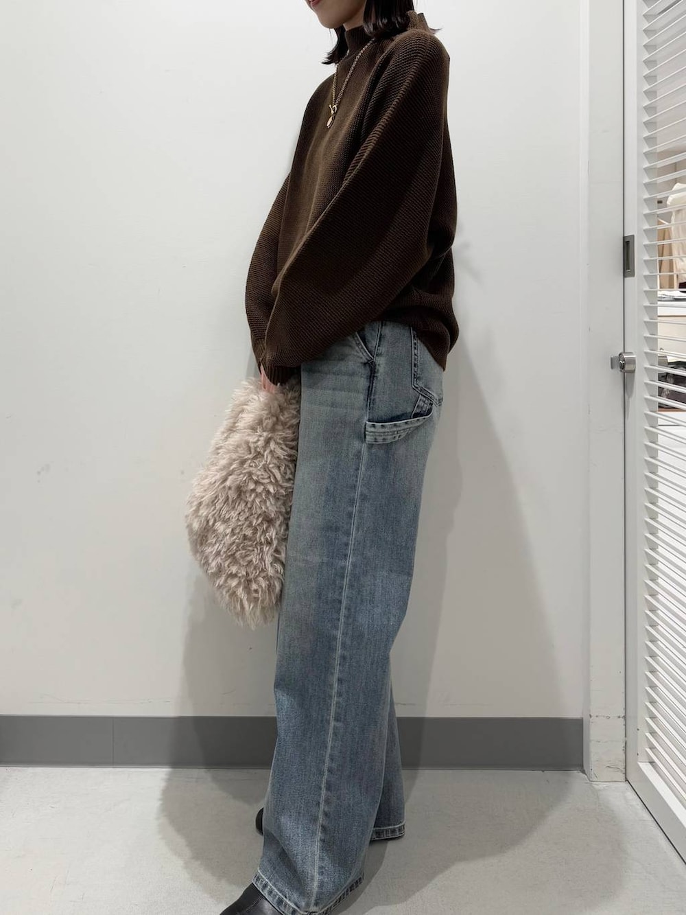 ブラウン系のトートバッグ、ブラック系のブーツ、ブルー系のデニムパンツを着用したレディースの冬コーディネートの2枚目の写真