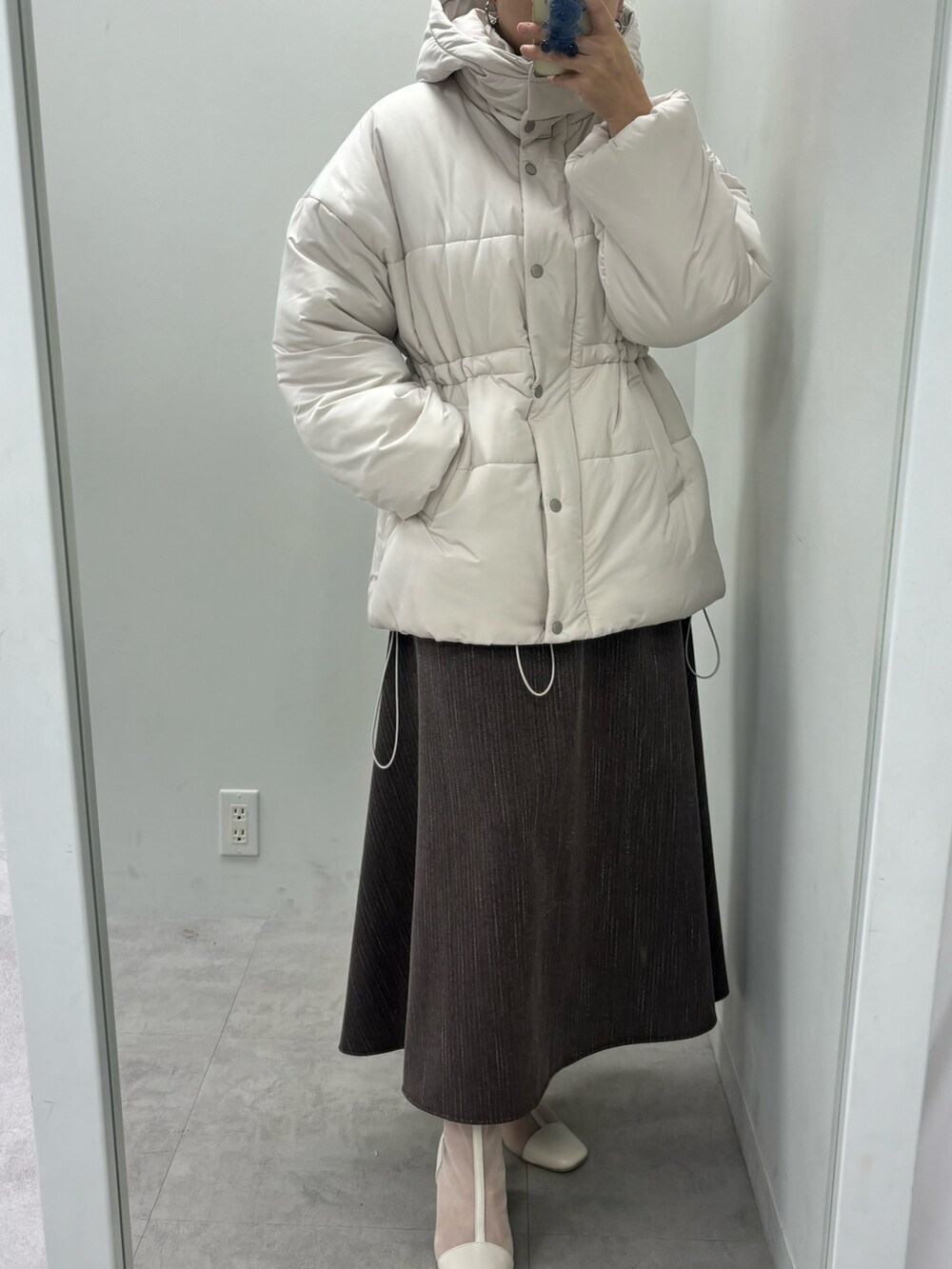 ブラウン系のスカート、ホワイト系のニット/セーター、ベージュ系のダウンジャケット/コートを着用したレディースの秋コーディネートの4枚目の写真