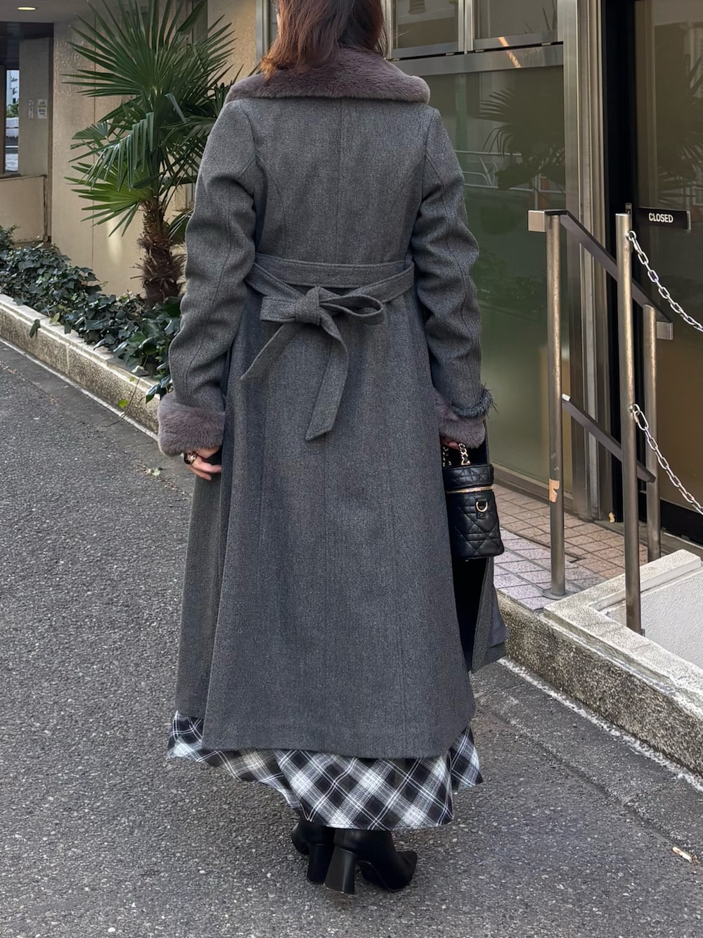 グレー系のステンカラーコート、ブラック系のブーツ、グレー系のワンピースを着用したレディースの冬コーディネートの3枚目の写真