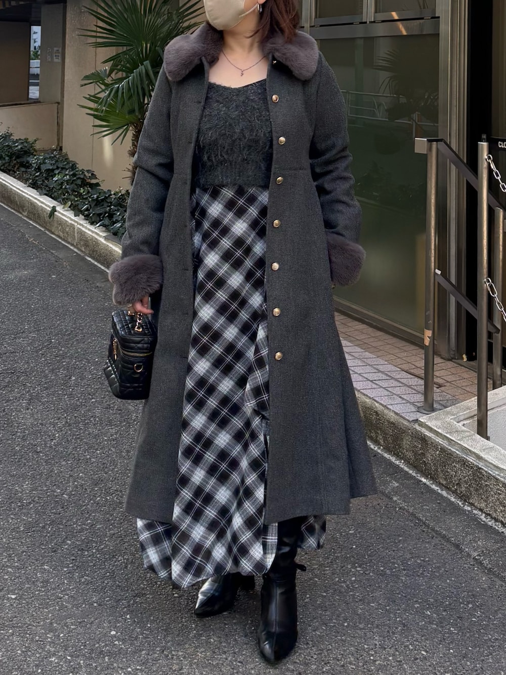 グレー系のステンカラーコート、ブラック系のブーツ、グレー系のワンピースを着用したレディースの冬コーディネートの2枚目の写真