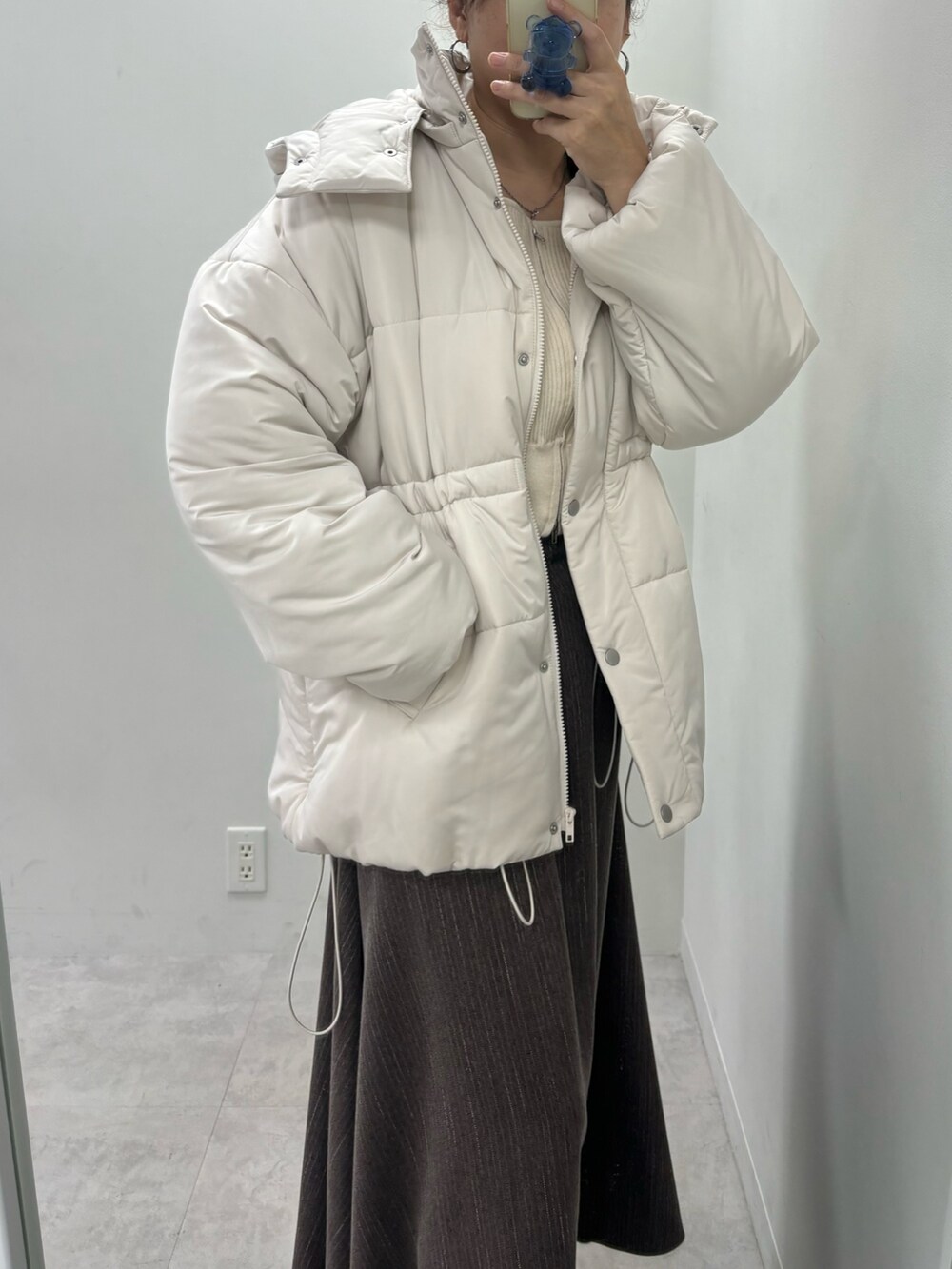 ブラウン系のスカート、ベージュ系のダウンジャケット/コート、ホワイト系のニット/セーターを着用したレディースの冬コーディネートの2枚目の写真