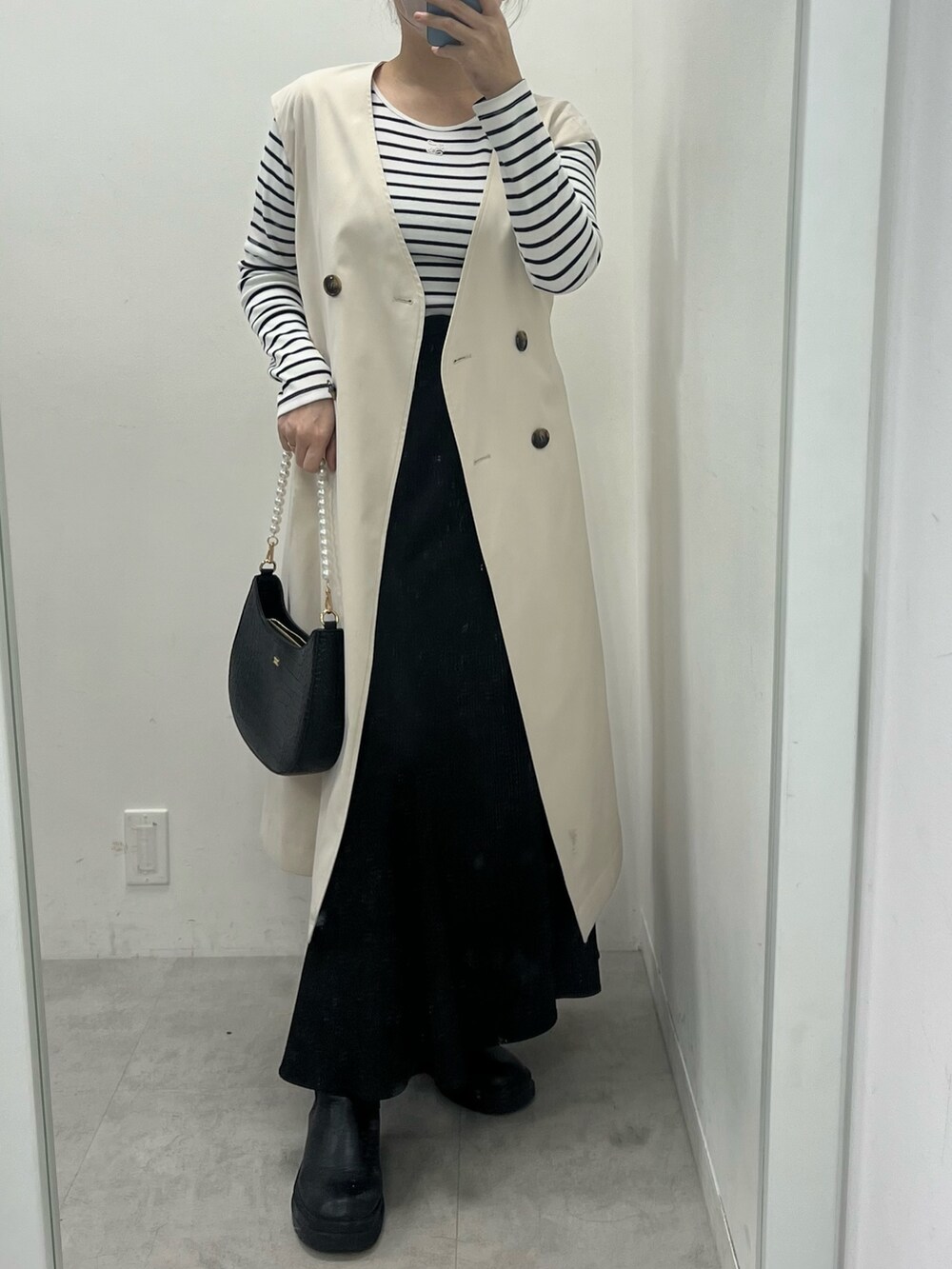 ブラック系のスカート、ホワイト系のTシャツ/カットソー、ベージュ系のトレンチコートを着用したレディースの冬コーディネートの2枚目の写真