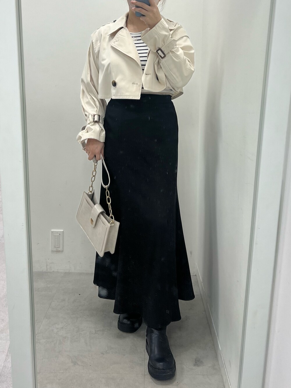 ブラック系のスカート、ホワイト系のトレンチコート、ブラック系のブーツを着用したレディースの春コーディネートの3枚目の写真