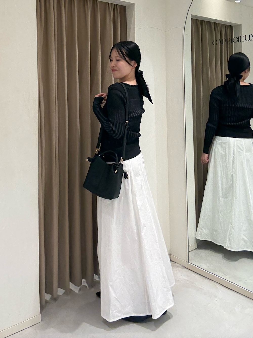 ホワイト系のスカート、ブラック系のカーディガン/ボレロ、ブラック系のショルダーバッグを着用したレディースの春コーディネートの2枚目の写真