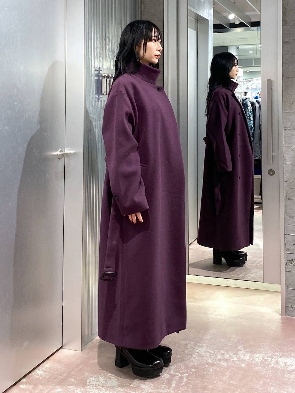 パープル系のチェスターコート、ブラック系のブーツ、パープル系のスカートを着用したレディースの冬コーディネートの4枚目の写真