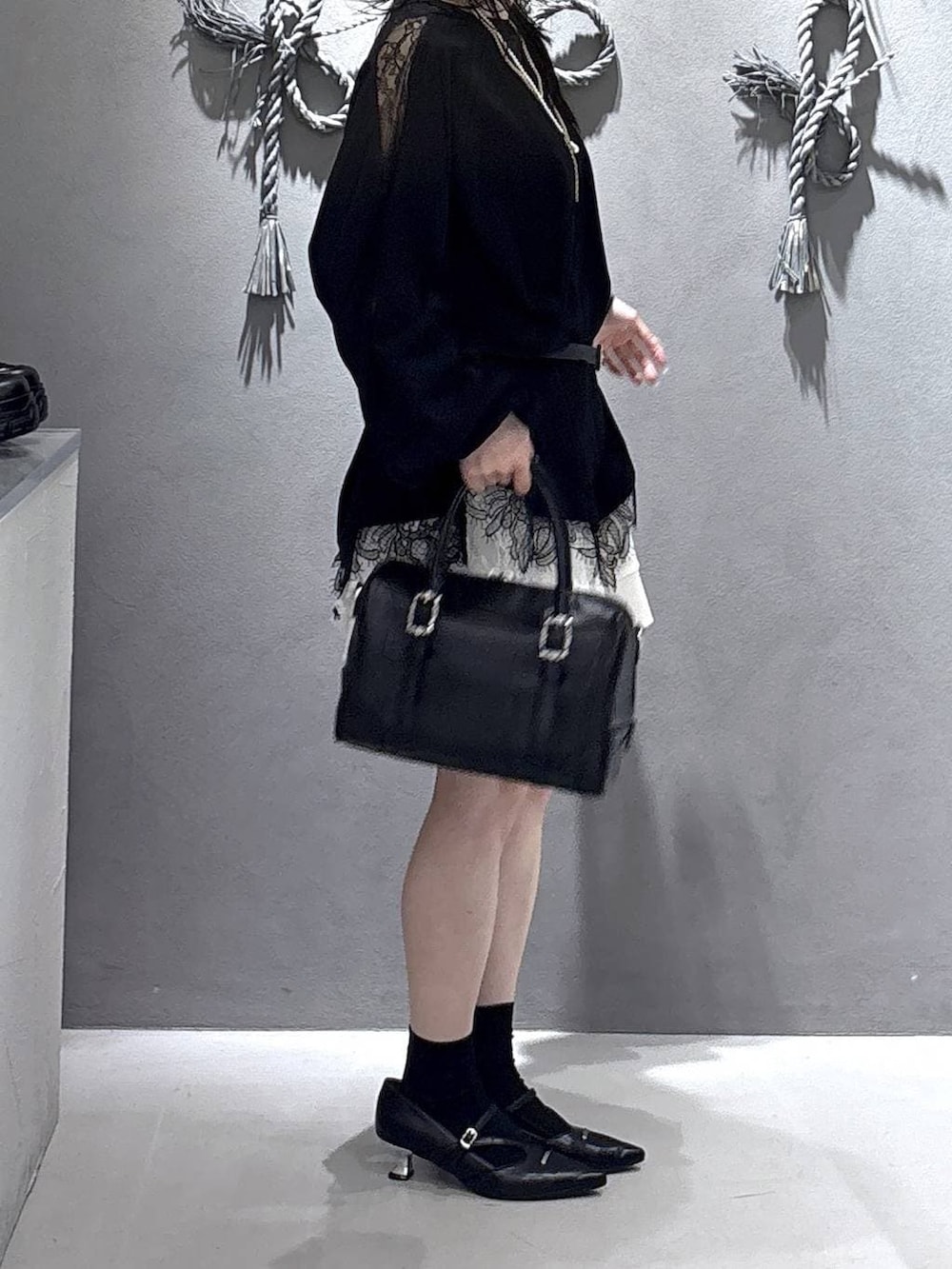 ブラック系のボストンバッグ、ブラック系のパンプス、ホワイト系のスカートを着用したレディースの冬コーディネートの4枚目の写真