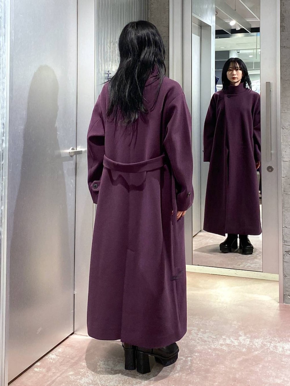 パープル系のチェスターコート、ブラック系のブーツ、パープル系のスカートを着用したレディースの冬コーディネートの3枚目の写真