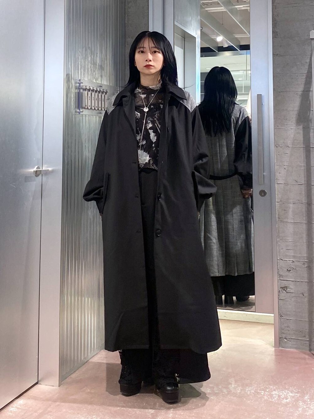ブラック系のブーツ、ブラック系のステンカラーコート、ブラック系のTシャツ/カットソーを着用したレディースの秋コーディネートの2枚目の写真