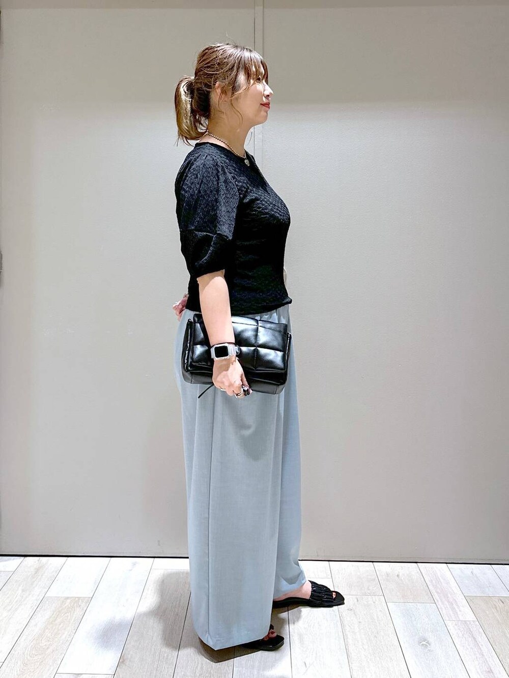 ブラック系のショルダーバッグ、ブラック系のTシャツ/カットソー、ブルー系のスラックスを着用したレディースの夏コーディネートの2枚目の写真