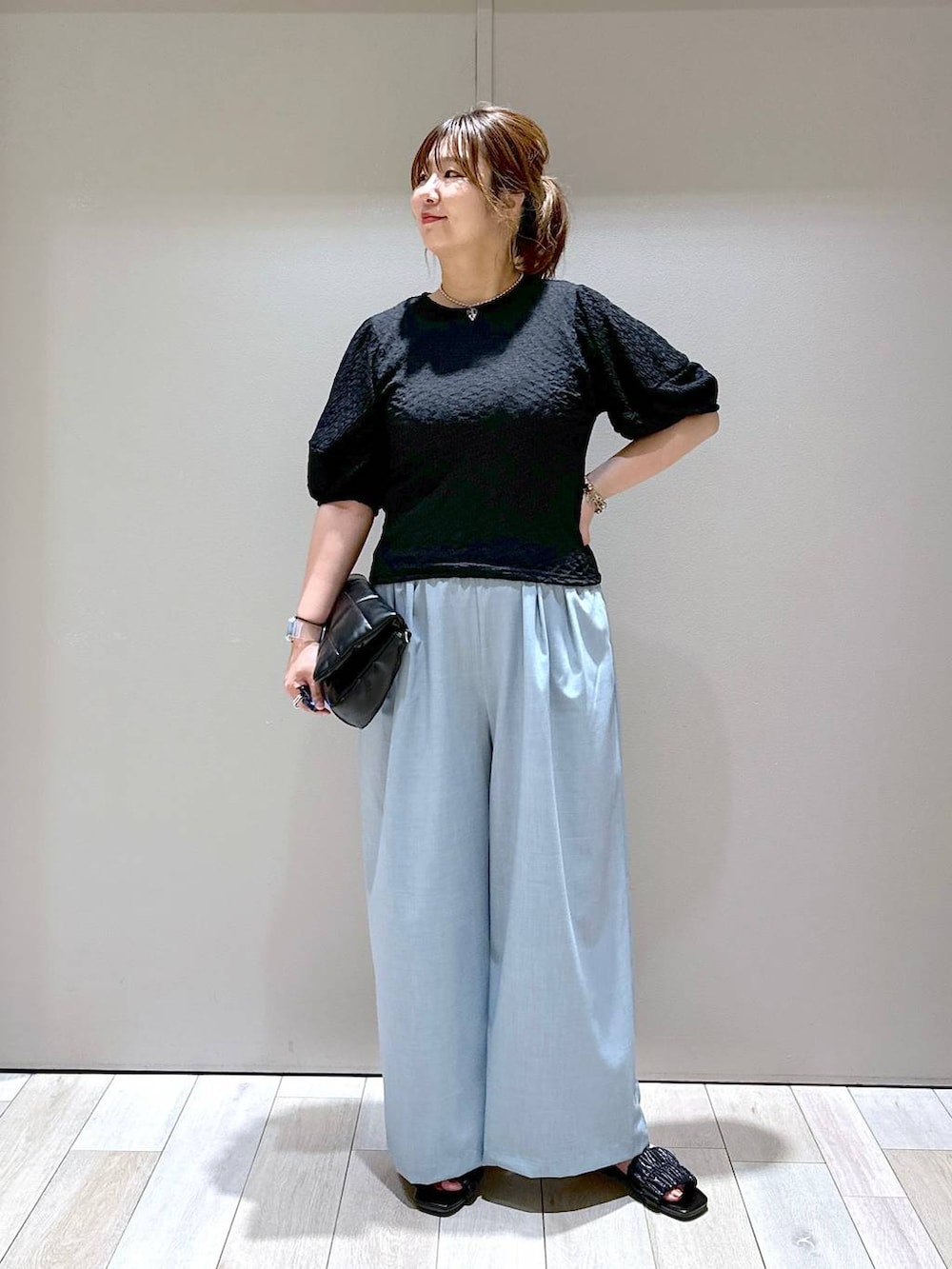 ブラック系のショルダーバッグ、ブラック系のTシャツ/カットソー、ブルー系のスラックスを着用したレディースの夏コーディネートの3枚目の写真