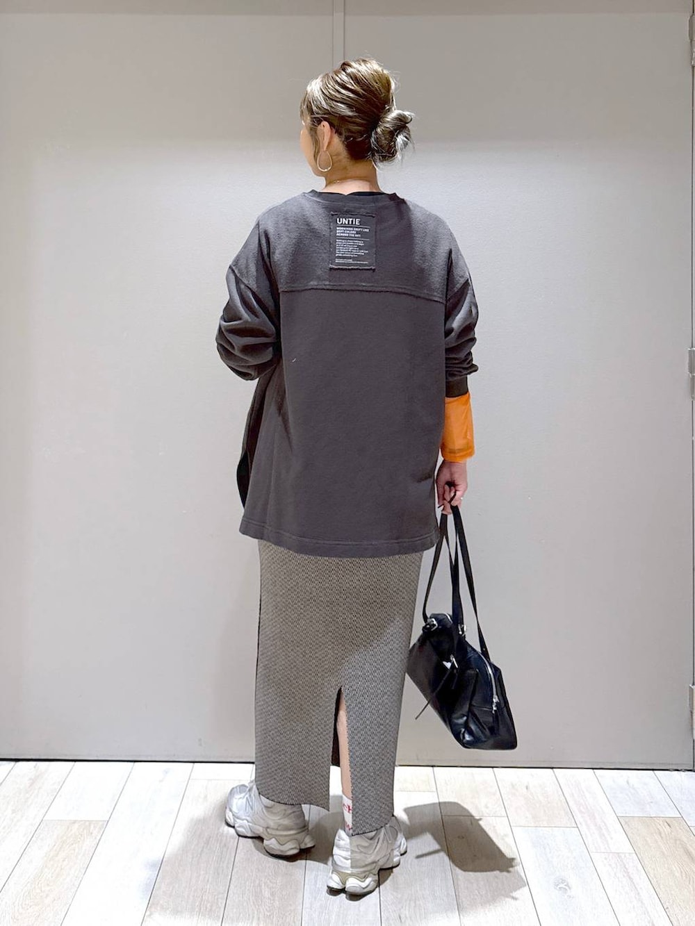 オレンジ系のTシャツ/カットソー、ブラック系のスカート、ブラック系のボストンバッグを着用したレディースの秋コーディネートの3枚目の写真