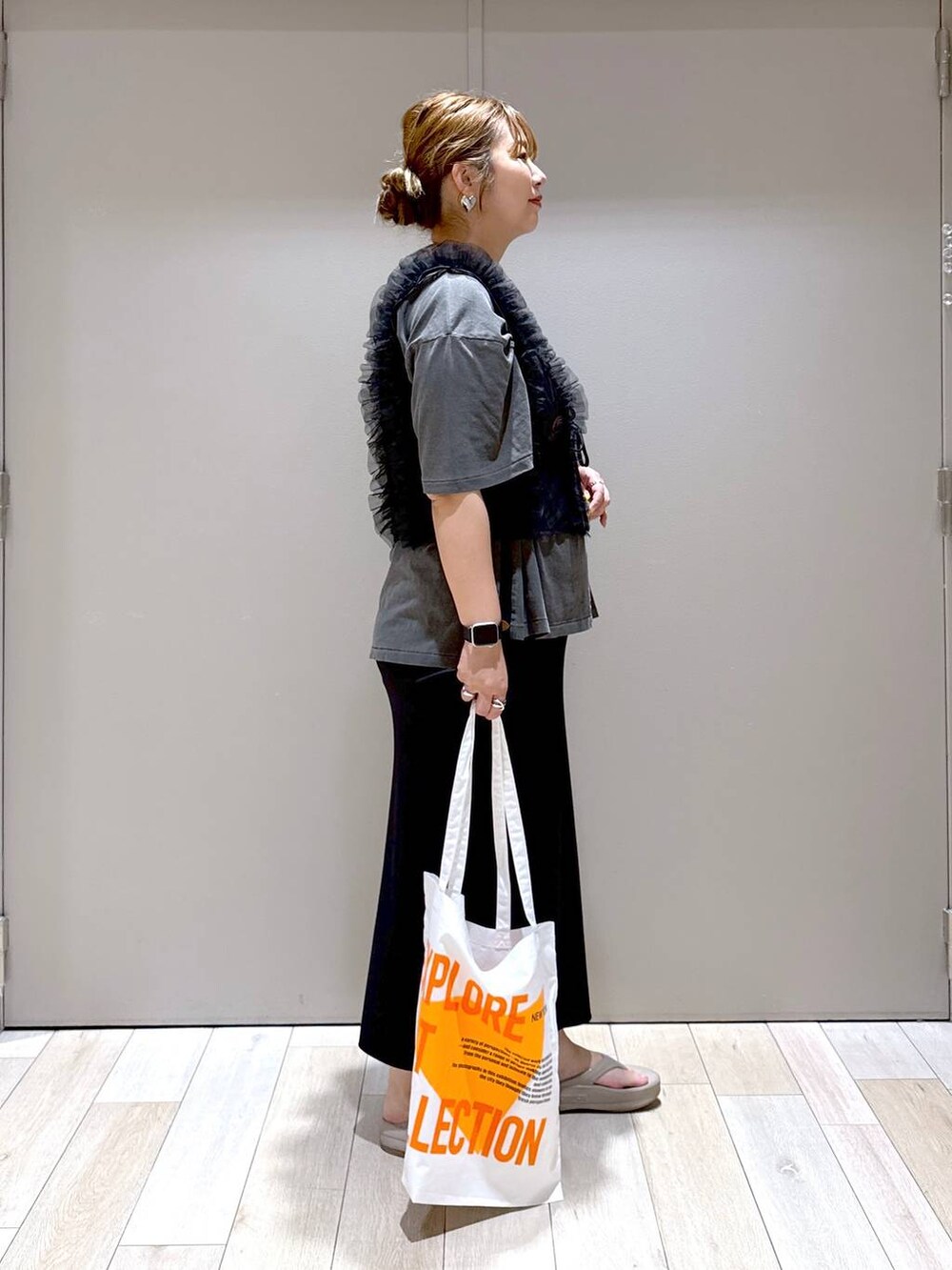 オレンジ系のトートバッグ、ブラック系のベスト、ベージュ系のサンダルを着用したレディースの夏コーディネートの2枚目の写真