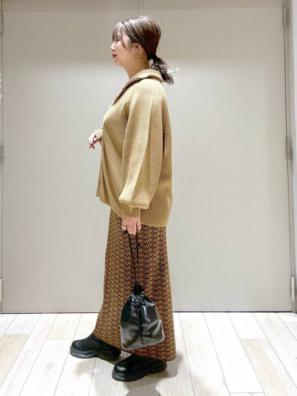 ブラウン系のスカート、ブラウン系のニット/セーター、ブラック系のブーツを着用したレディースの冬コーディネートの2枚目の写真