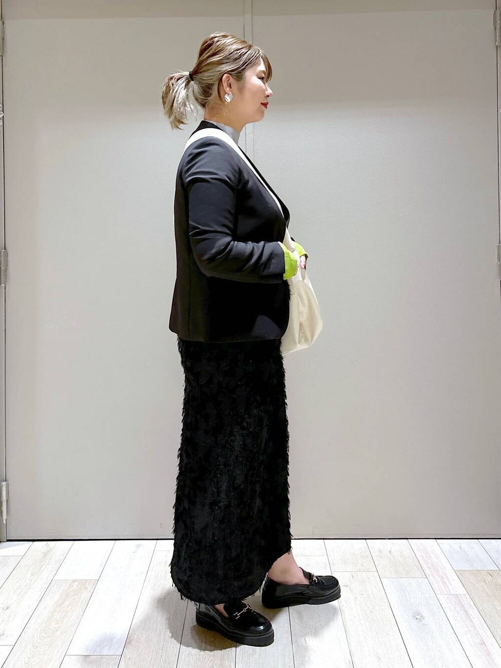 ブラック系のスカート、ホワイト系のショルダーバッグ、グレー系のニット/セーターを着用したレディースの冬コーディネートの2枚目の写真