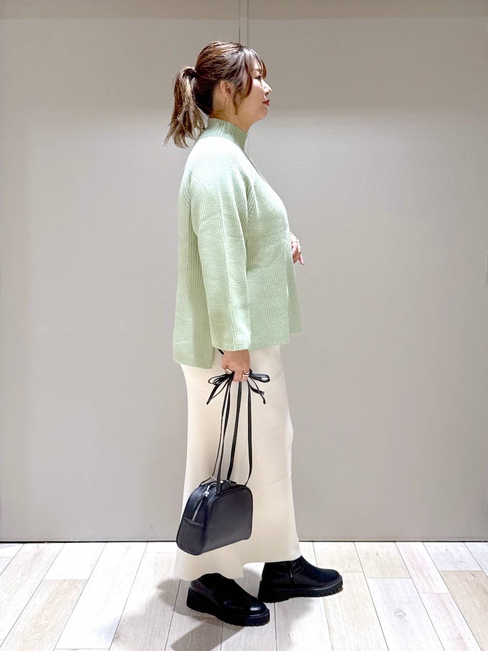 ブラック系のスカート、ブラック系のブーツ、ホワイト系のニット/セーターを着用したレディースの冬コーディネートの2枚目の写真