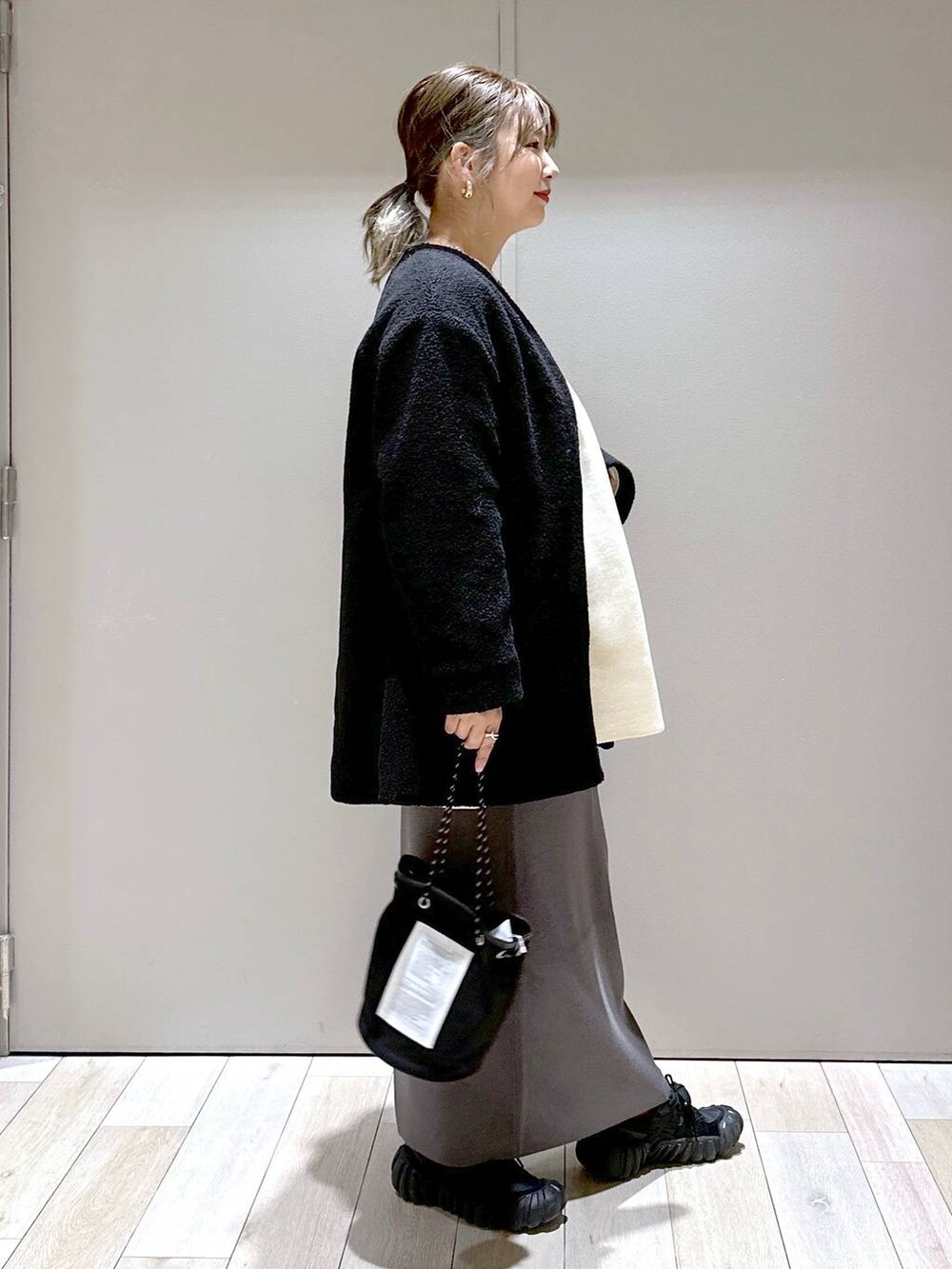 グレー系のスカート、ブラック系のノーカラーコート、ホワイト系のワンピースを着用したレディースの秋コーディネートの2枚目の写真