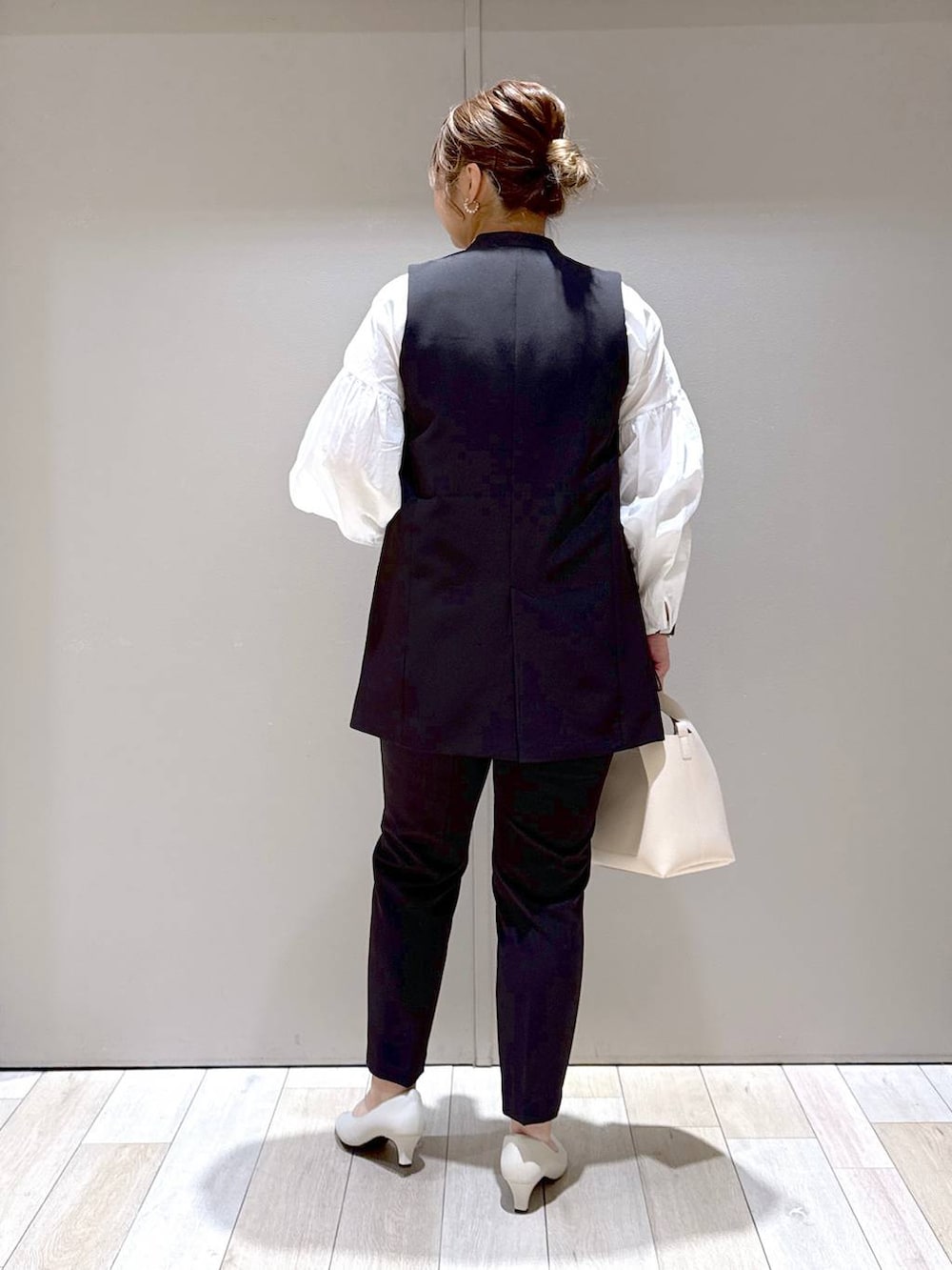 ブラック系のスーツパンツ、ブラック系のスーツベスト、ホワイト系のパンプスを着用したレディースの冬コーディネートの3枚目の写真