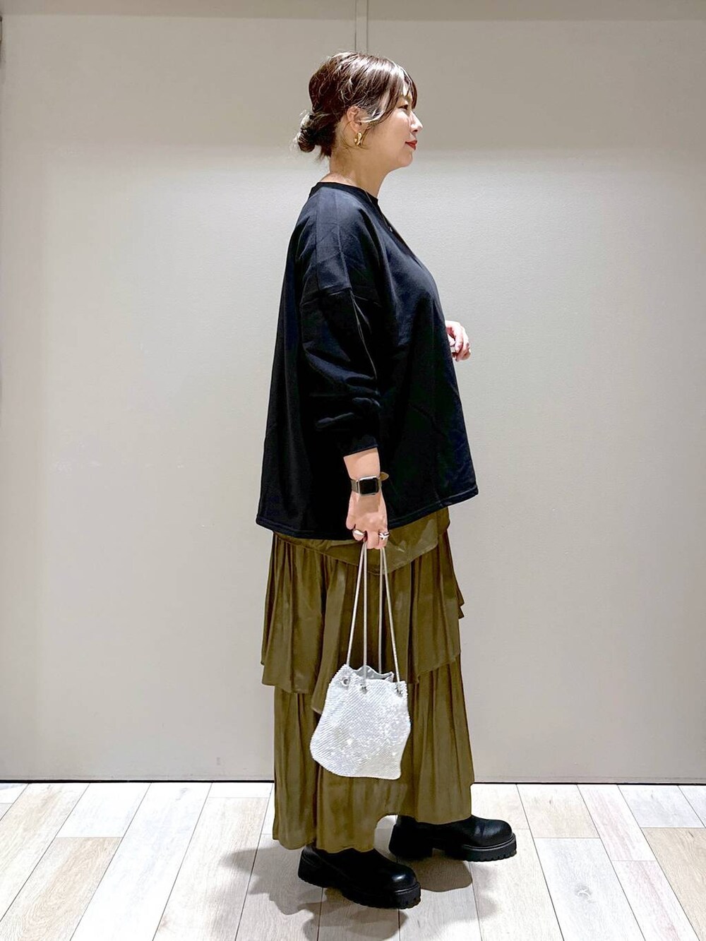 シルバー系のショルダーバッグ、ブラック系のブーツ、グリーン系のスカートを着用したレディースの秋コーディネートの2枚目の写真