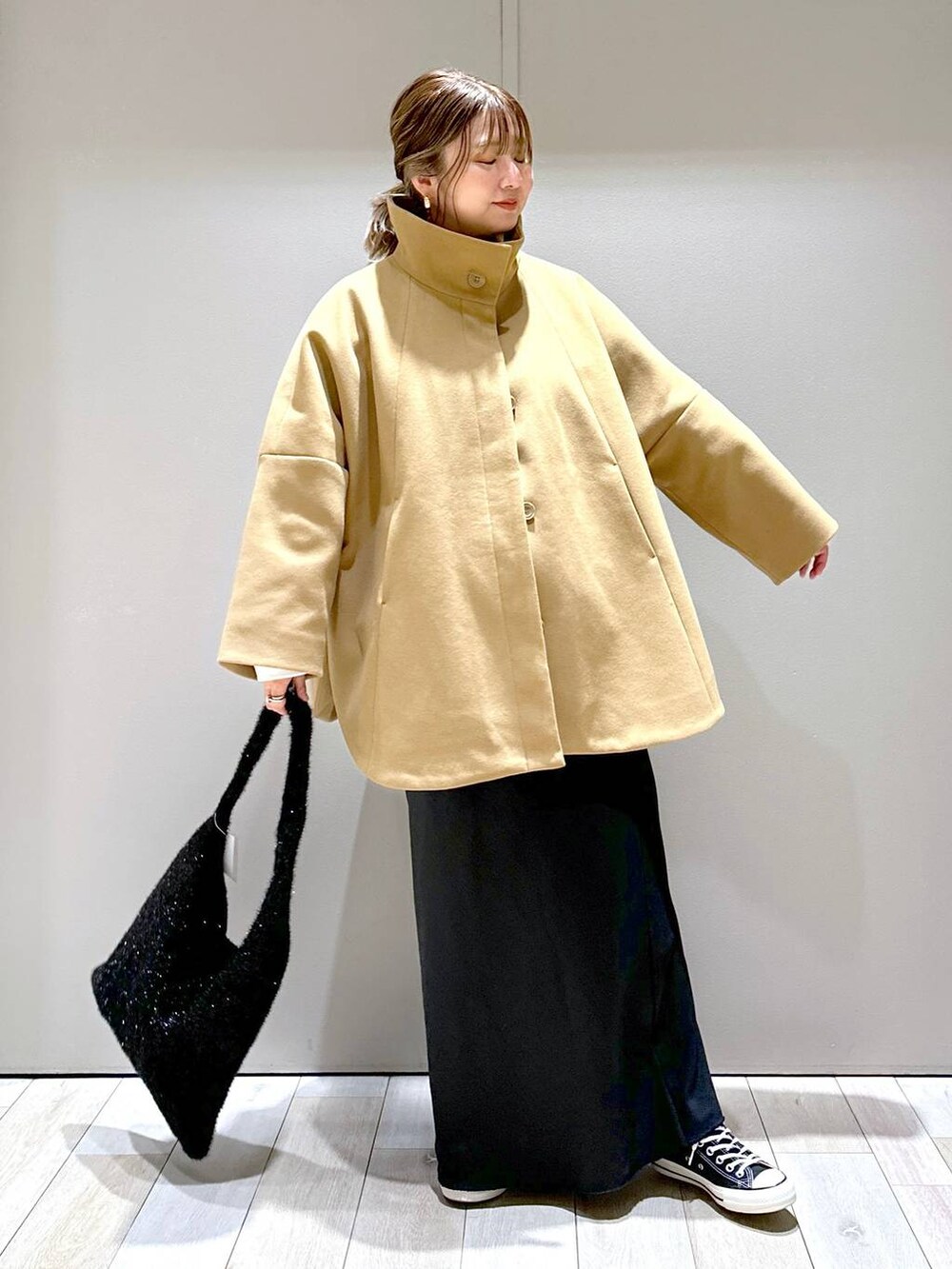 ブラウン系のポンチョ、ブラック系のショルダーバッグ、ブラック系のスカートを着用したレディースの秋コーディネートの4枚目の写真