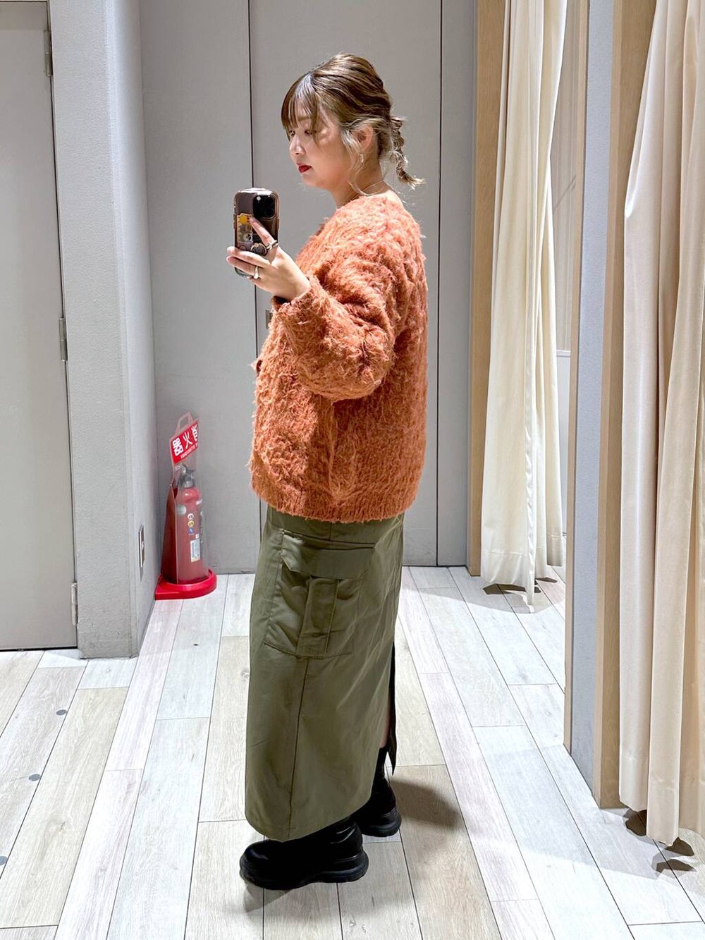 オレンジ系のカーディガン/ボレロ、グリーン系のスカート、ブラック系のブーツを着用したレディースの冬コーディネートの2枚目の写真