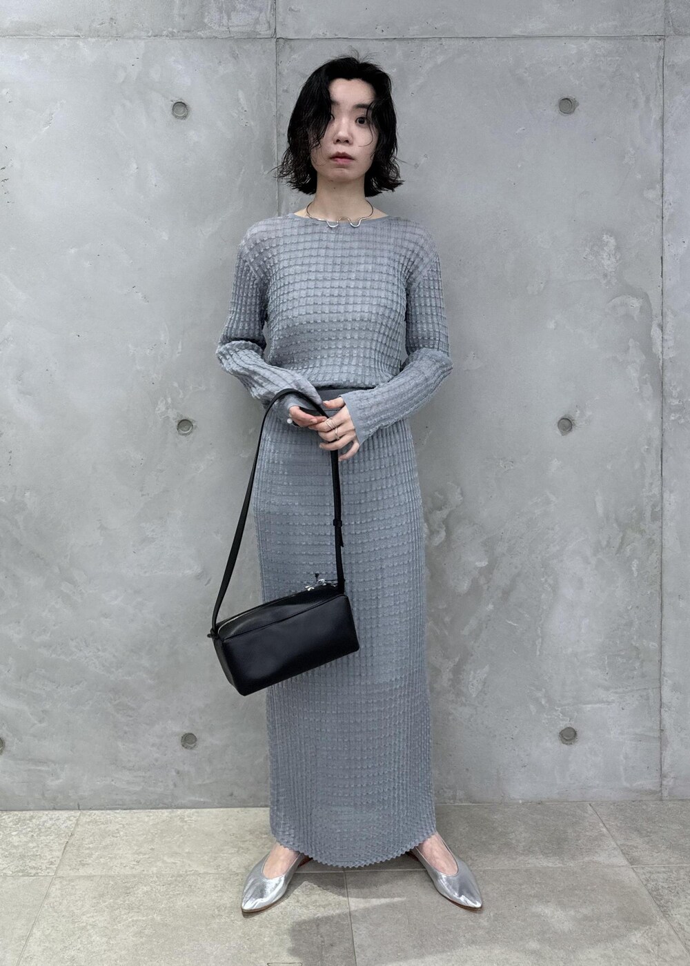 グレー系のニット/セーター、グレー系のスカート、ブラック系のショルダーバッグを着用したレディースの春コーディネートの2枚目の写真