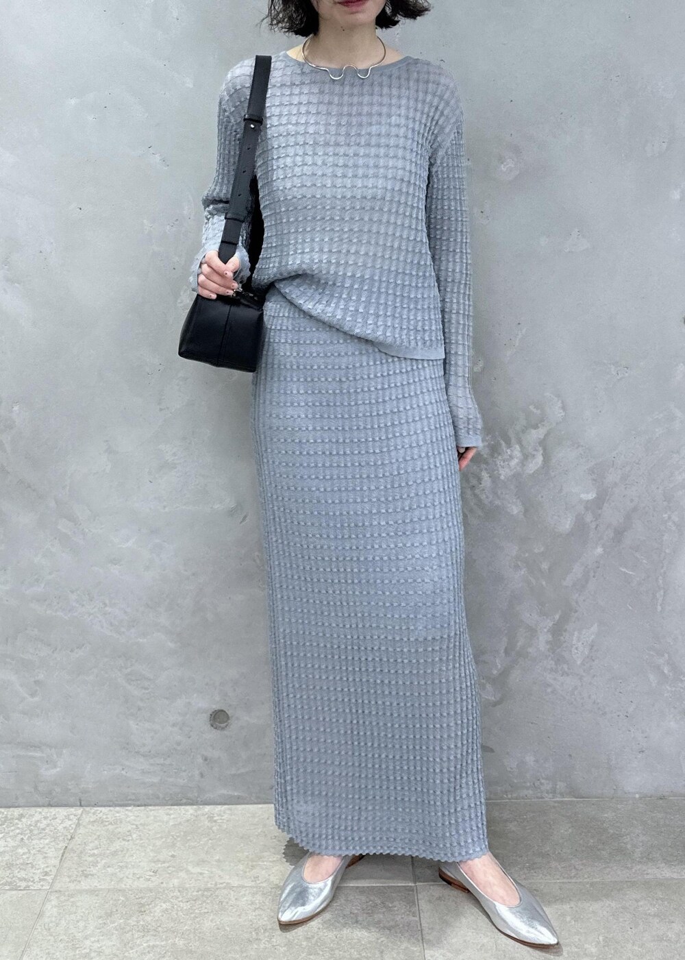 グレー系のニット/セーター、グレー系のスカート、ブラック系のショルダーバッグを着用したレディースの春コーディネートの3枚目の写真