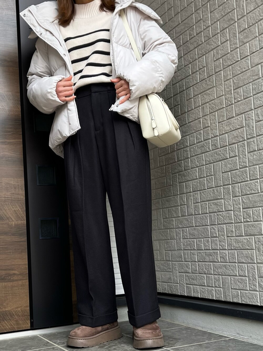 ブラック系のパンツ、ブラウン系のブーツ、ホワイト系のバッグを着用したレディースの冬コーディネートの2枚目の写真