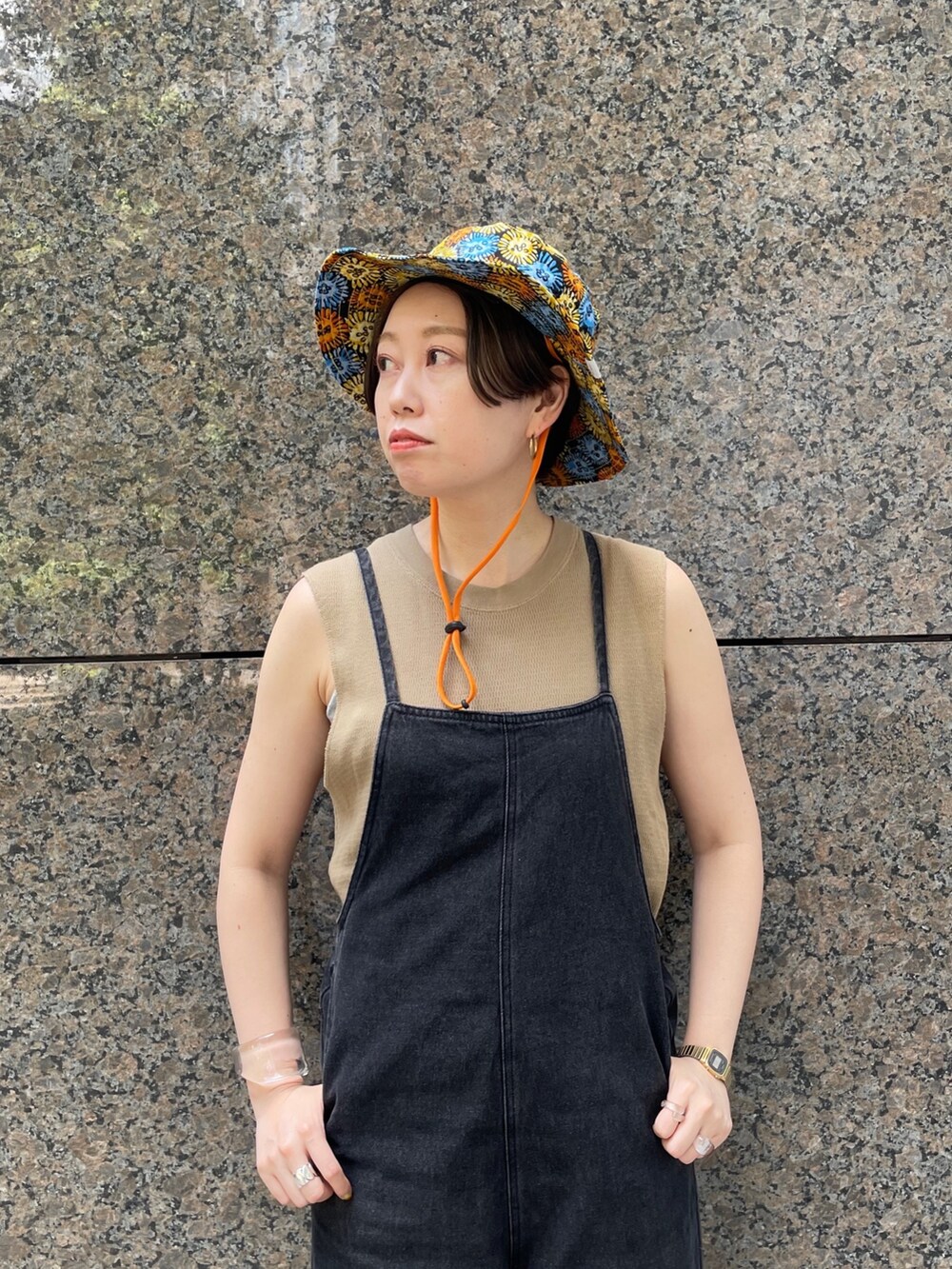 ブラック系のサロペット/オーバーオール、ブラック系のサンダル、オレンジ系のハットを着用したレディースの春コーディネートの3枚目の写真