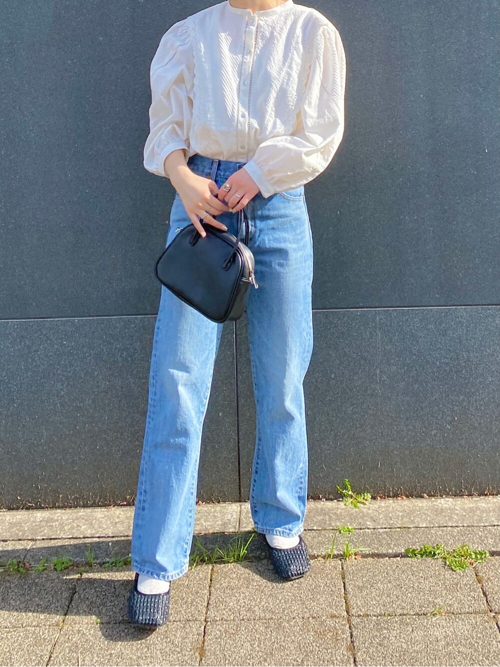 ブラック系のハンドバッグ、ブラック系のパンプス、ブルー系のデニムパンツを着用したレディースの春コーディネートの2枚目の写真