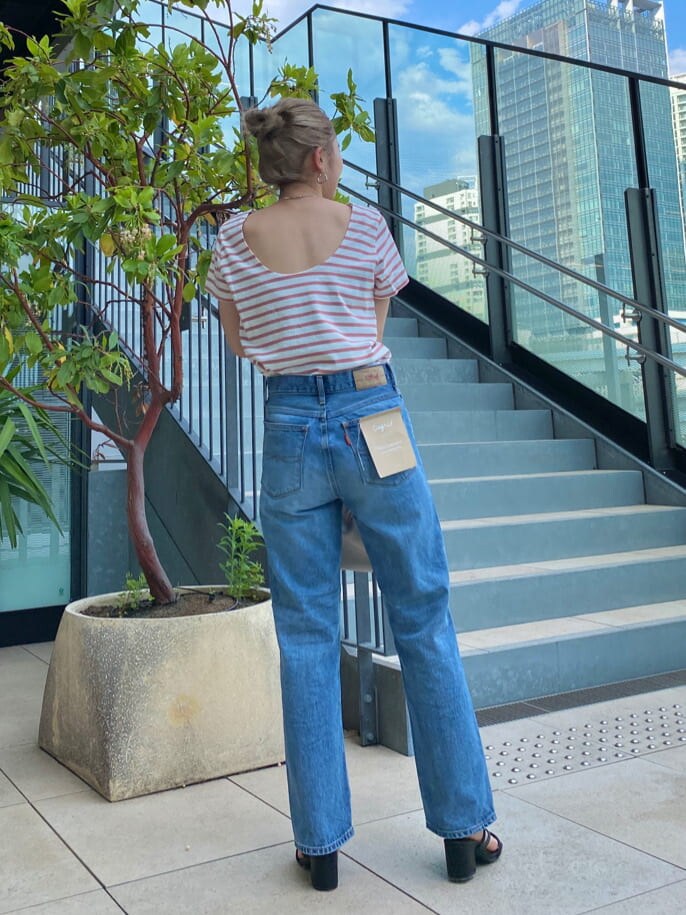 ブルー系のデニムパンツ、ブラック系のサンダル、ピンク系のハンドバッグを着用したレディースの夏コーディネートの2枚目の写真