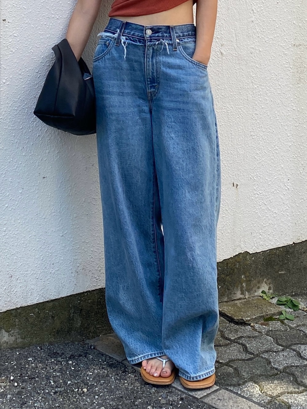 オレンジ系のタンクトップ、ブルー系のデニムパンツ、ブラック系のハンドバッグを着用したレディースの夏コーディネートの4枚目の写真