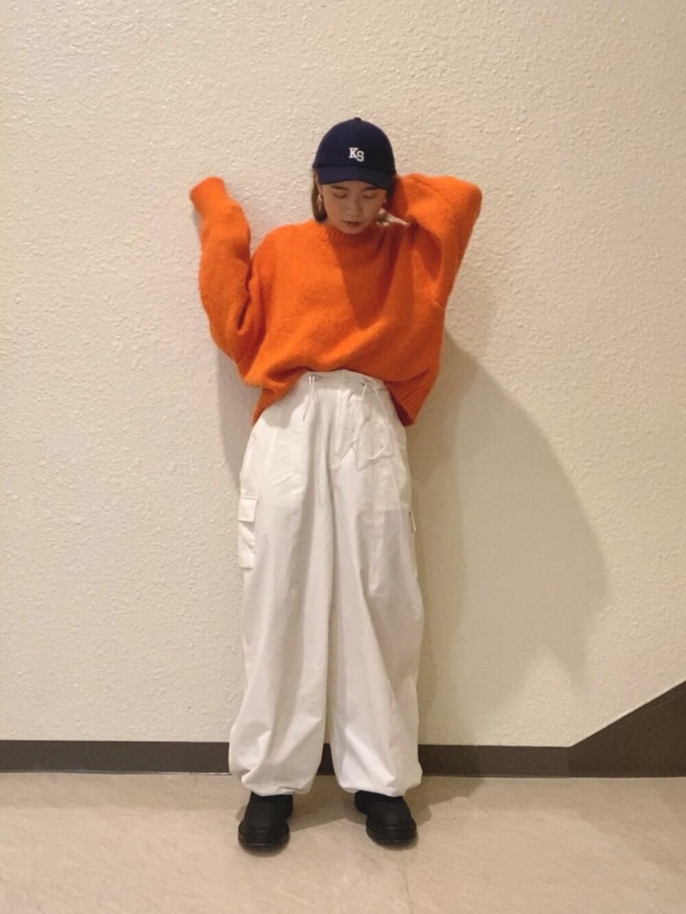 オレンジ系のニット/セーター、ホワイト系のカーゴパンツ、ブラック系のブーツを着用したレディースの冬コーディネートの2枚目の写真