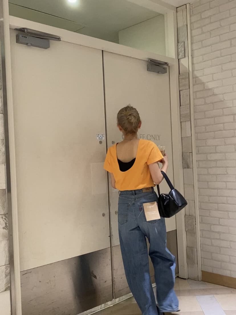 オレンジ系のTシャツ/カットソー、ブラック系のサンダル、ブルー系のデニムパンツを着用したレディースの夏コーディネートの4枚目の写真