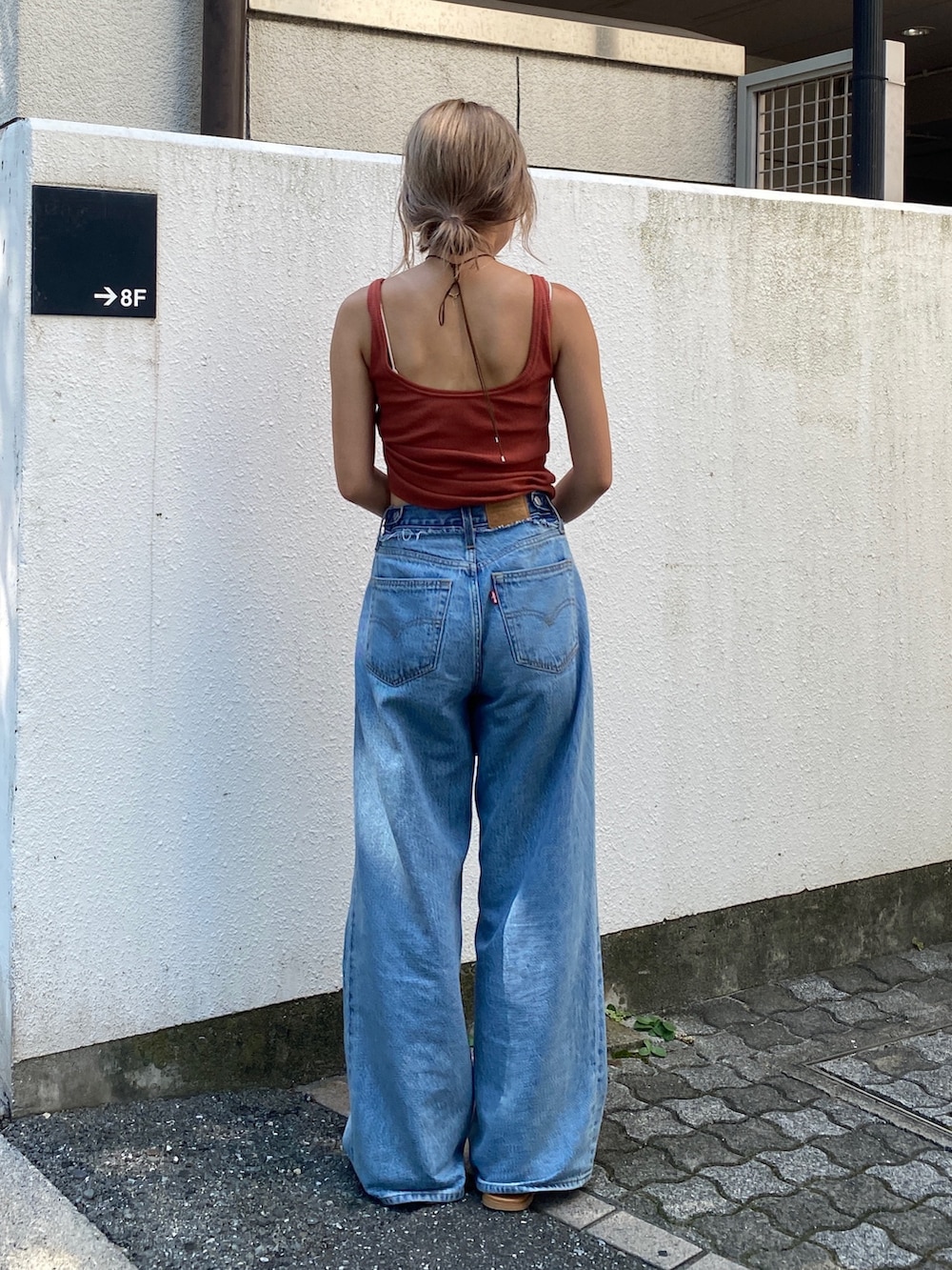 オレンジ系のタンクトップ、ブルー系のデニムパンツ、ブラック系のハンドバッグを着用したレディースの夏コーディネートの3枚目の写真