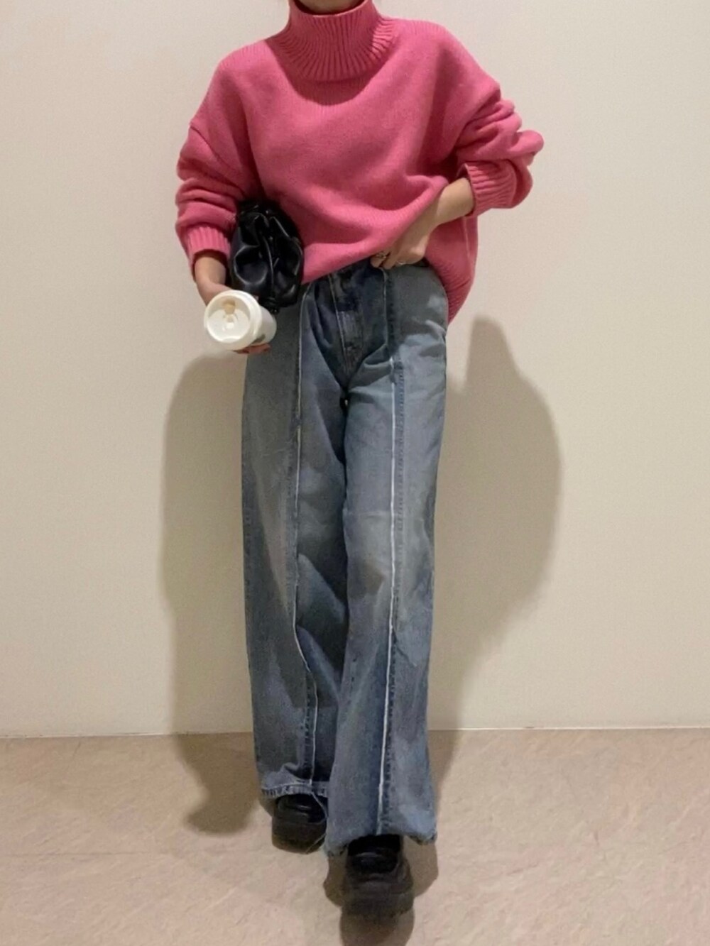 ピンク系のニット/セーター、ブルー系のデニムパンツ、ブラック系のクラッチバッグを着用したレディースの冬コーディネートの2枚目の写真