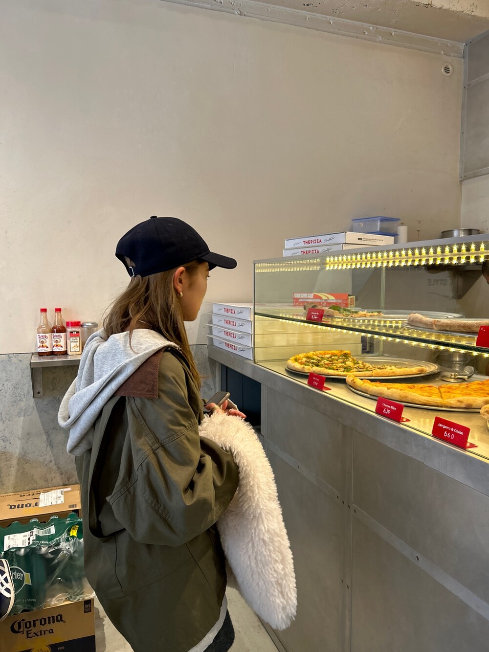 グレー系のパーカー、ホワイト系のハンドバッグ、ベージュ系のカバーオールを着用したレディースの冬コーディネートの3枚目の写真