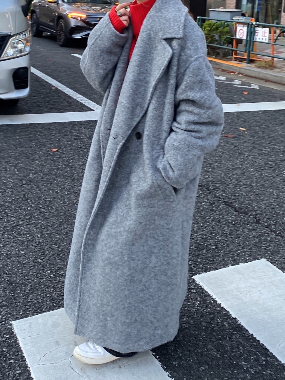 レッド系のニット/セーター、グレー系のチェスターコート、ブルー系のデニムパンツを着用したレディースの冬コーディネートの2枚目の写真