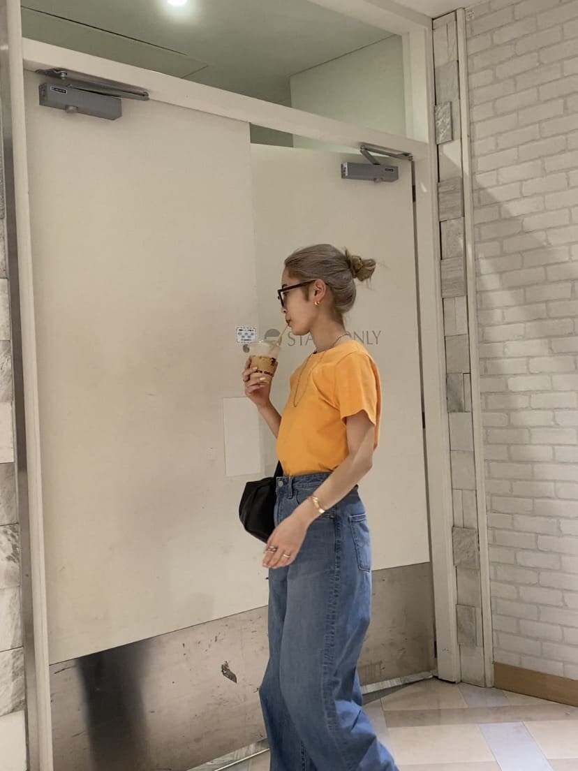 オレンジ系のTシャツ/カットソー、ブラック系のサンダル、ブルー系のデニムパンツを着用したレディースの夏コーディネートの2枚目の写真