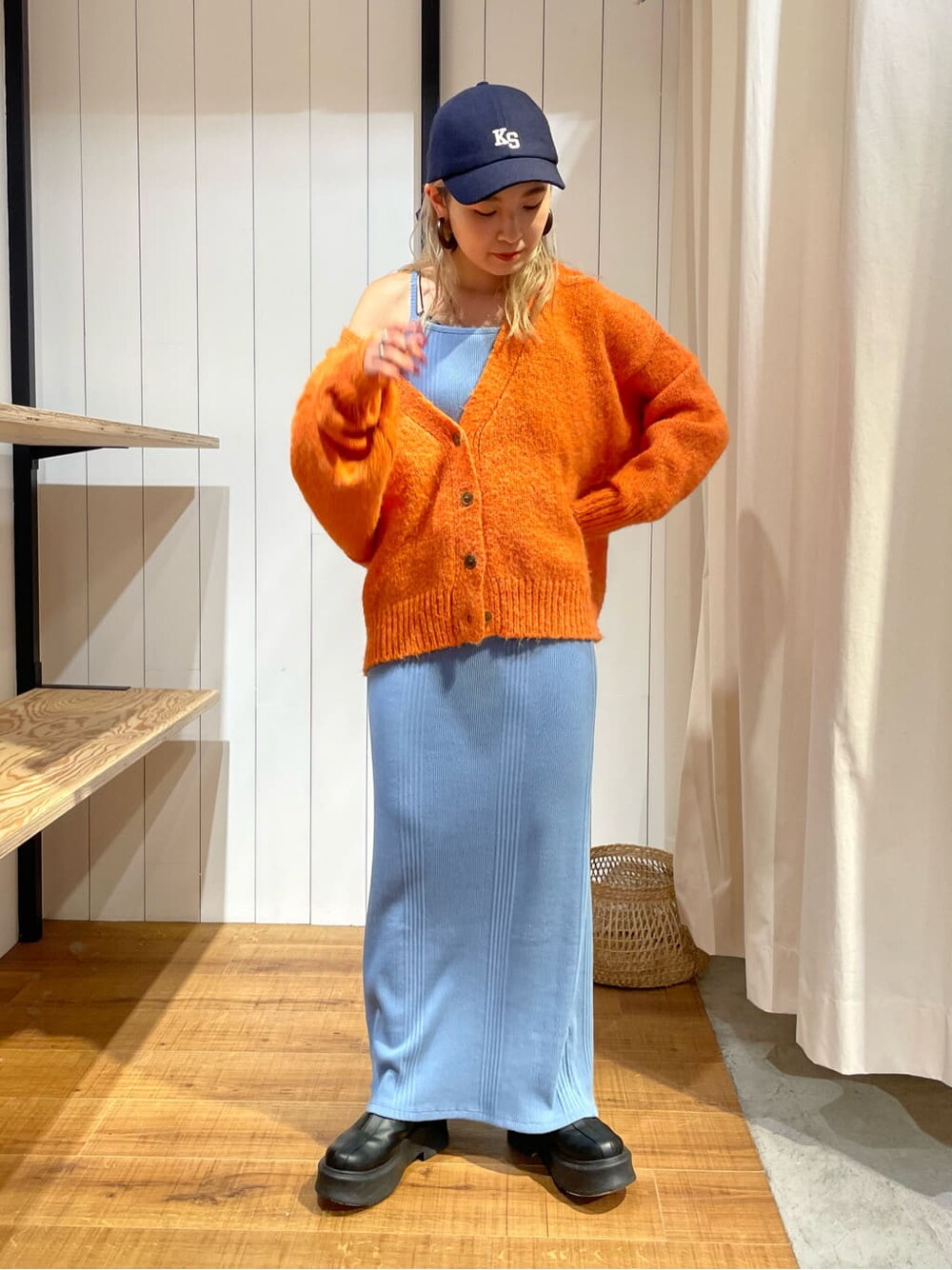 オレンジ系のカーディガン/ボレロ、ブラック系のブーツ、ブルー系のワンピースを着用したレディースの秋コーディネートの2枚目の写真