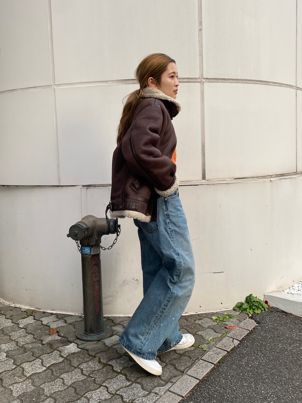 オレンジ系のニット/セーター、ブラウン系のムートンコート、ブルー系のデニムパンツを着用したレディースの冬コーディネートの2枚目の写真