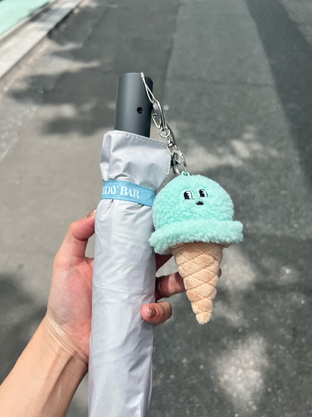 グリーン系のショルダーバッグ、グレー系の折りたたみ傘を着用したレディースの夏コーディネートの2枚目の写真